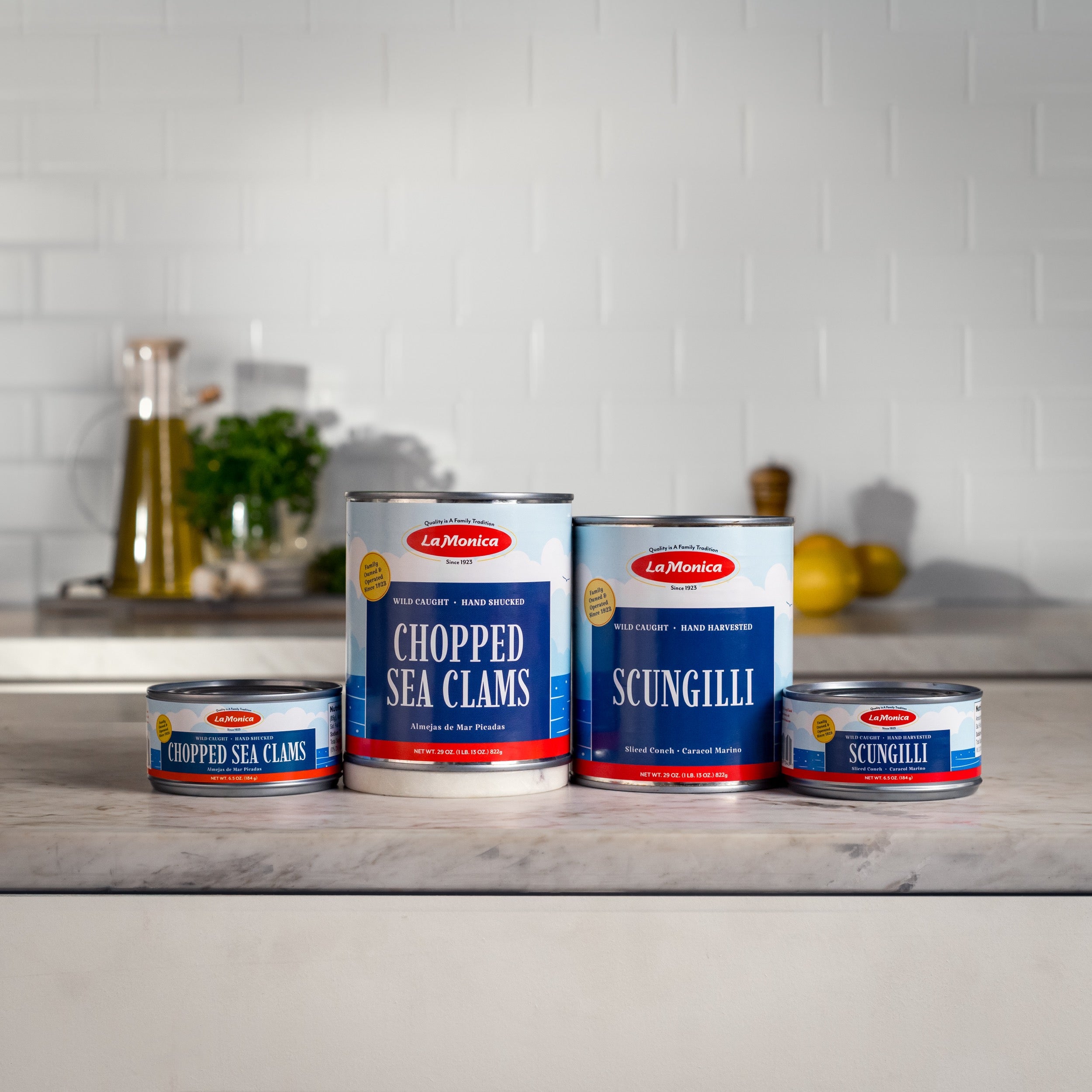 Four cans of LaMonica products on a kitchen counter with a white tiled wall background.