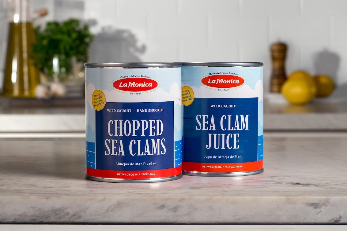 Two cans of LaMonica sea food products on a kitchen counter with a white tiled wall background.