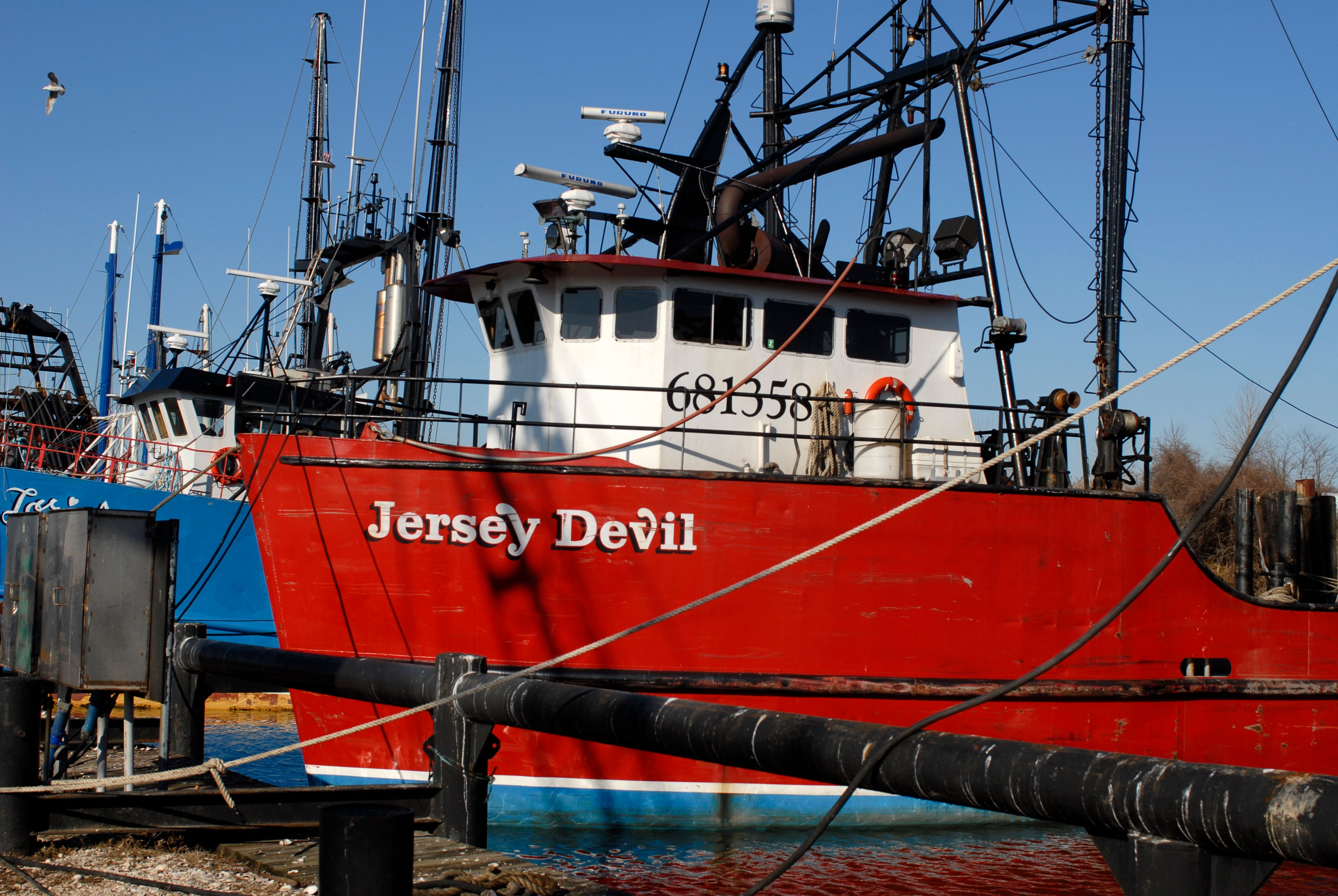 Red boat named 'Jersey Devil' docked at a pier with clear blue sky.