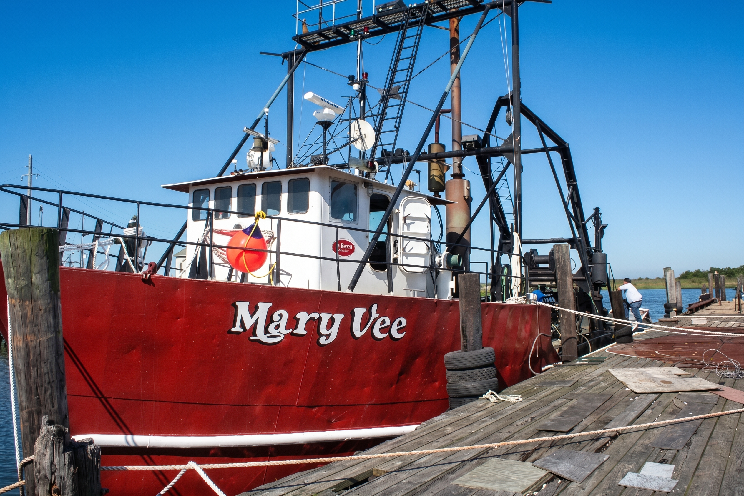 Red fishing boat named 'Mary Vee' docked at a pier with clear blue sky.