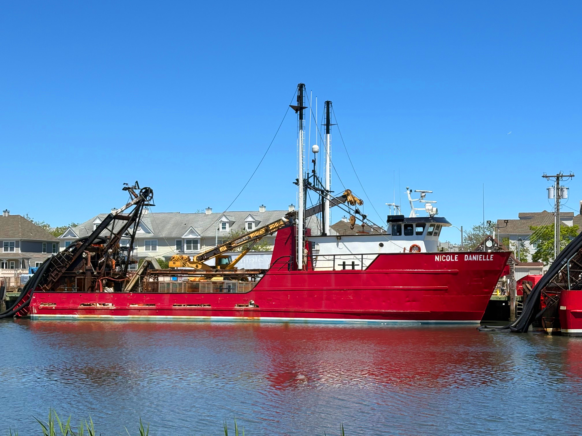 Red boat named 'Nicole Danielle' docked in a harbor with clear blue sky.
