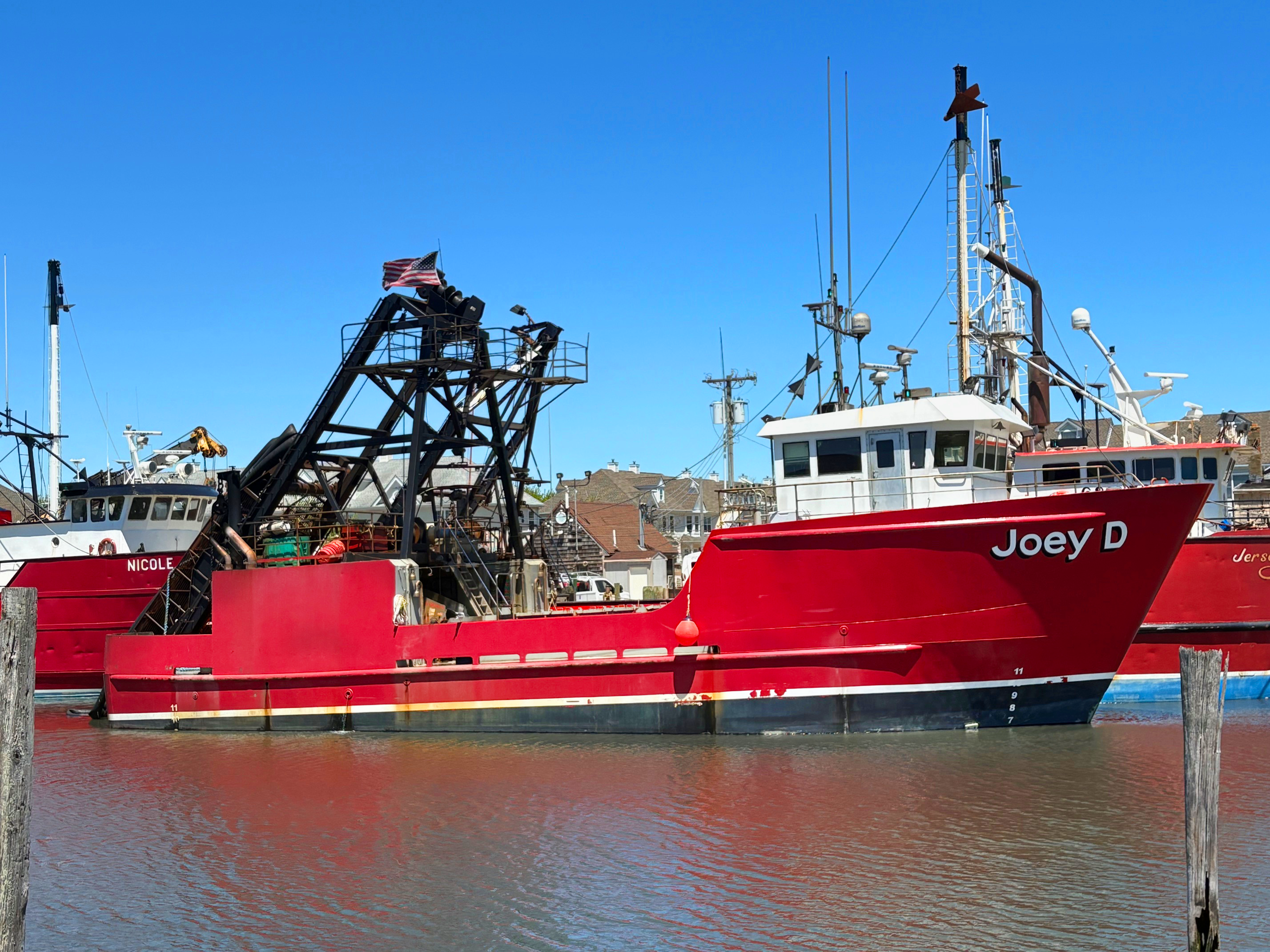 Red boat named 'Joey D' docked in a harbor with clear blue sky.